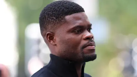 Reuters Thomas Partey wears a black zip-up collared sweater as he walks into Westminster Magistrates' Court, in London.