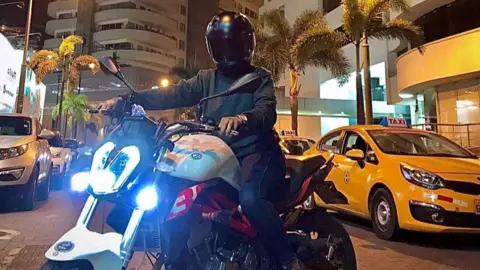 Submitted photo A woman wearing black, with her helmet obscuring her face, sits on a motorbike in traffic