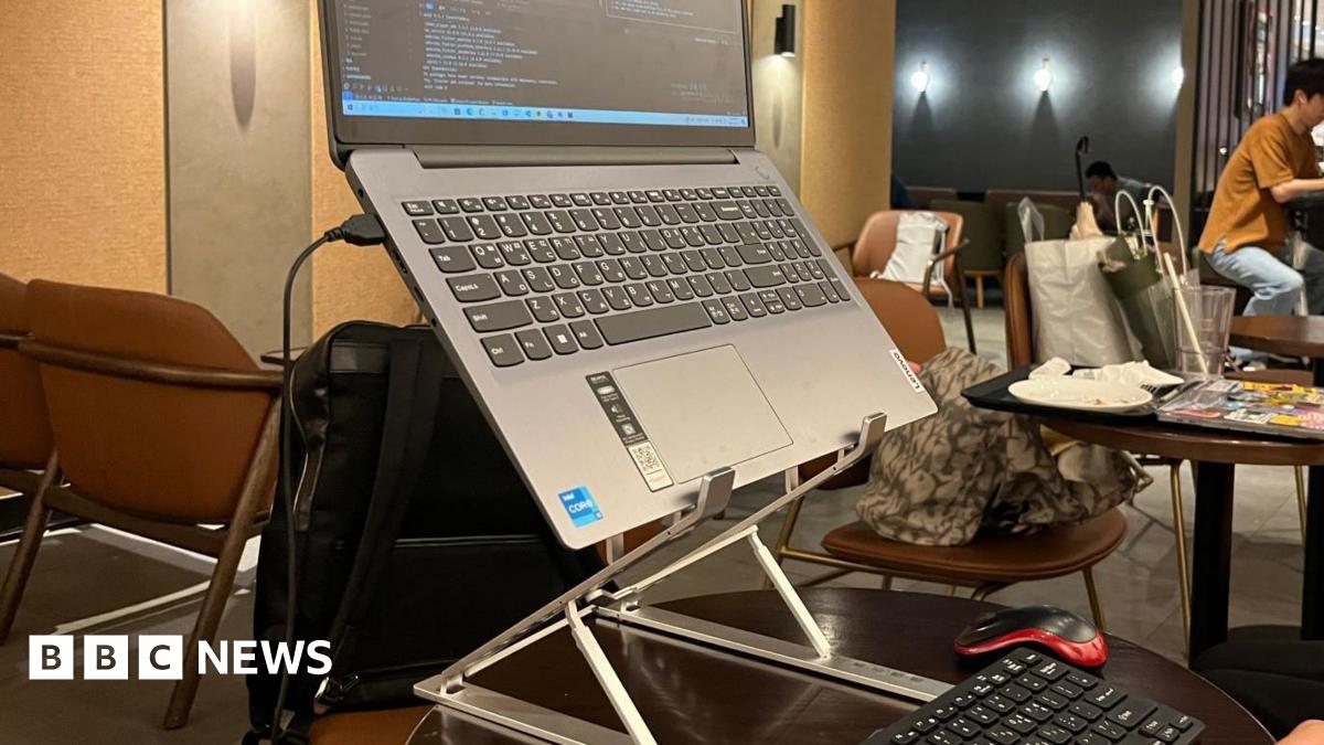 A laptop set up on a stand with a keyboard and mouse on a table in a Starbucks cafe.