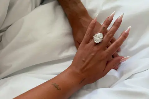 @Georginagio/Instagram A picture showing two people's arms on a bed, with Gio's huge engagement ring visible on her finger.
