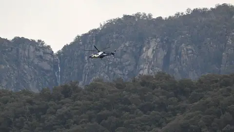 Getty Images A police helicopter flies over tree tops with a cliff face in the background