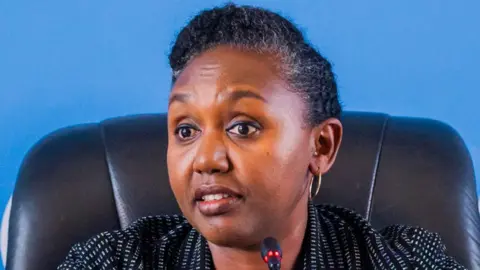 Anadolu Agency/Getty Images Rwanda government spokesperson Yolande Makole sits on a black chair before a microphone. She is wearing a white dotted black blazer.