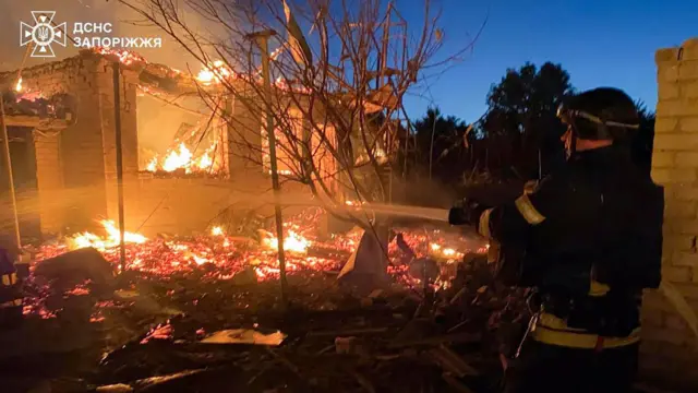 An emergency service worker directs a hose at a burning building