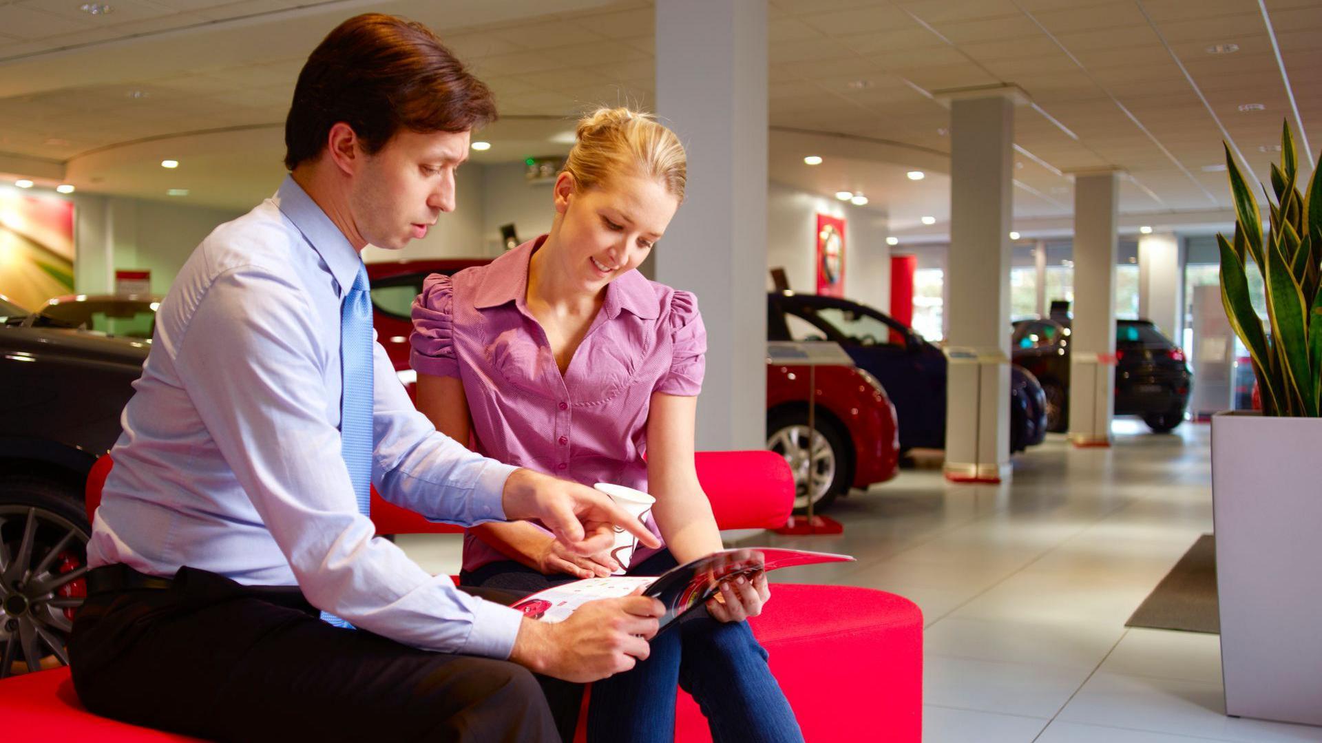 Sales representative with a young woman looking at paperwork in a car showroom