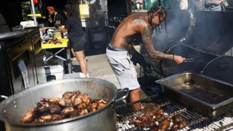 Reuters A man is bent over a barbecue with smoke coming out of it. In the foreground is grill with a meal dish of barbecued meat inside.