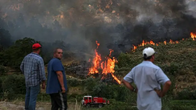Three men stand in front of a blazing wildfire in Portugal