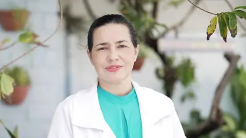 Felix Lima/BBC News Brasil Mardjane Lemos looks at the camera while wearing a turquoise blouse underneath a white doctor's coat.
