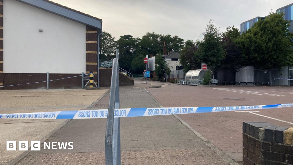A car park next to a supermarket, cordoned off with blue and white police tape. It's a cloudy day.