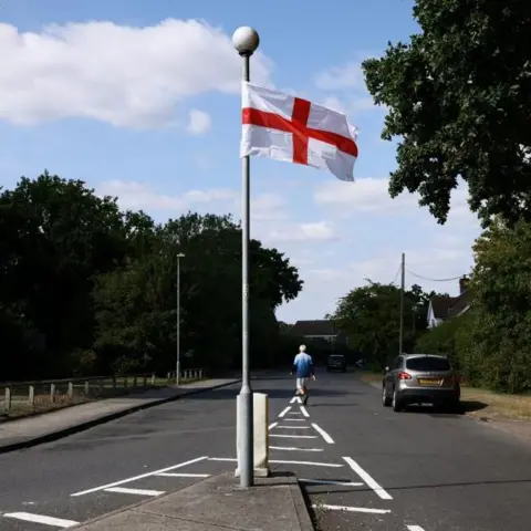 Reuters A flag of St George hangs from a lamppost on an island in the middle of an empty road, as a man walks down the road in the background.