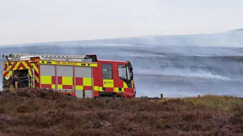 Getty Images A fire engine parked on Langdale Moor. Heather can be seen in the foreground, with smoke in the distance.