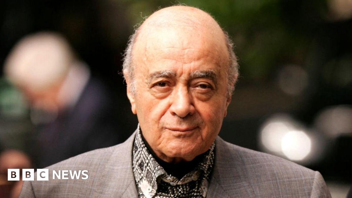 Mohamed Al Fayed in a grey suit with out of focus lights behind him