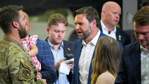 PA Media JD Vance, wearing a blue suit and white shirt, surrounded by US soldiers and their families.