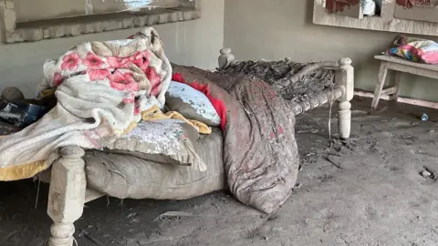 A bed and blankets covered in mud, inside a mud-flooded room