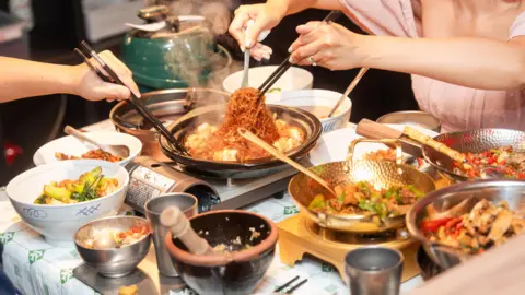 Nong Geng Ji Several dishes placed on a table at a branch of Nong Geng Ji, a popular Hunan restaurant chain in Singapore. Two customers (faces not in frame) are tucking into a spicy noodle dish at the centre of the table