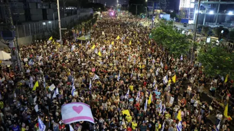 EPA An aerial image shows a crowd of protesters filling a street, some waving yellow banners and displaying a white flag with a pink heart, calling for the release of Israeli hostages in Tel Aviv, Israel on 9 August 2025.
