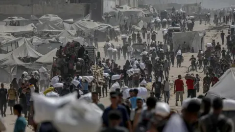 EPA A landscape image of a dirt track with a number of people walking and carrying white aid packages. Tents can also be seen.
