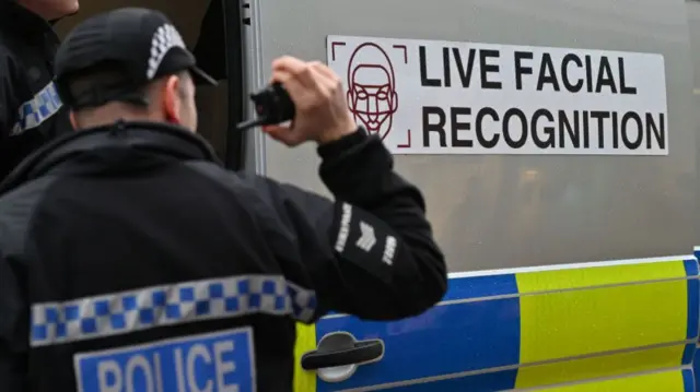 A police officer holding a radio stands outside a live facial recognition van in Southend, Essex, in 2024