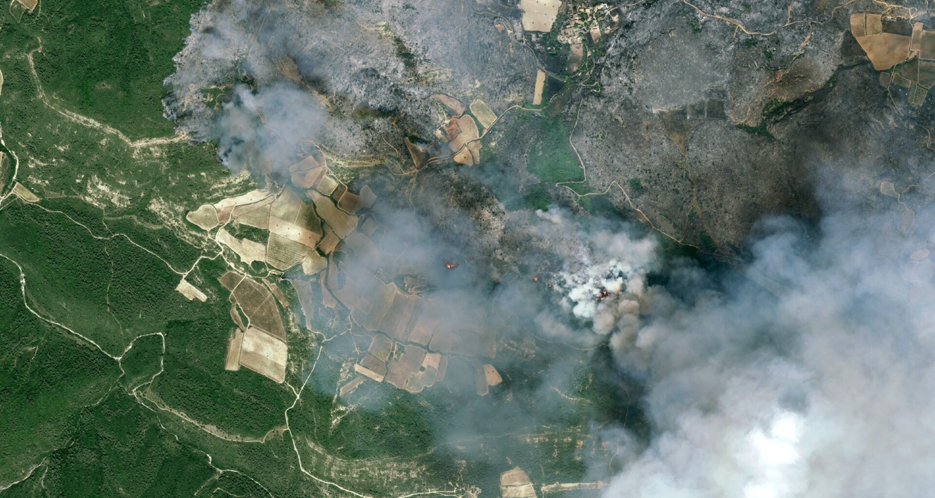 fire and smoke rolls through a green countryside as seen from space