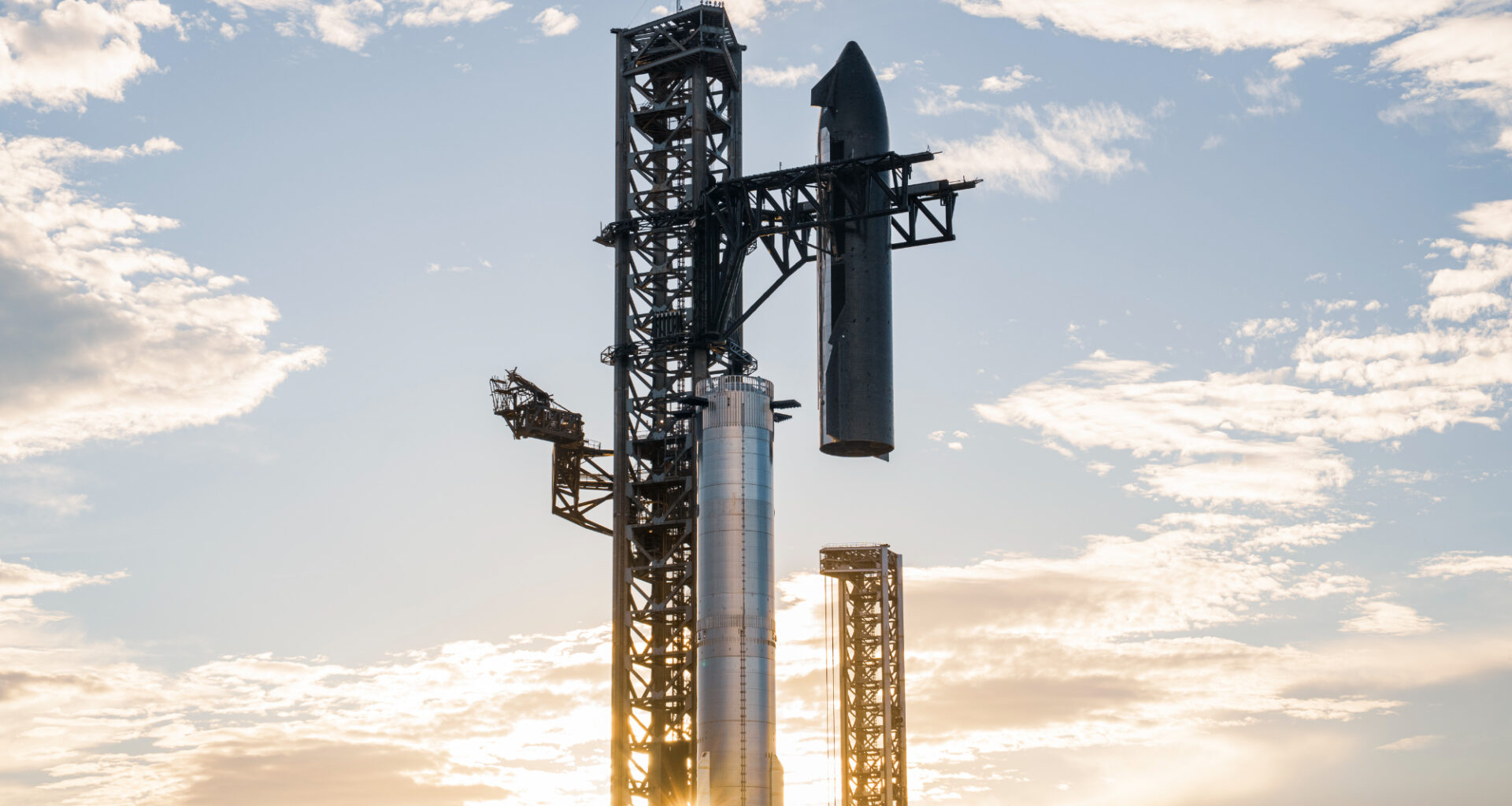 a giant silver spacecraft is stacked atop its silver booster by a metal launch tower