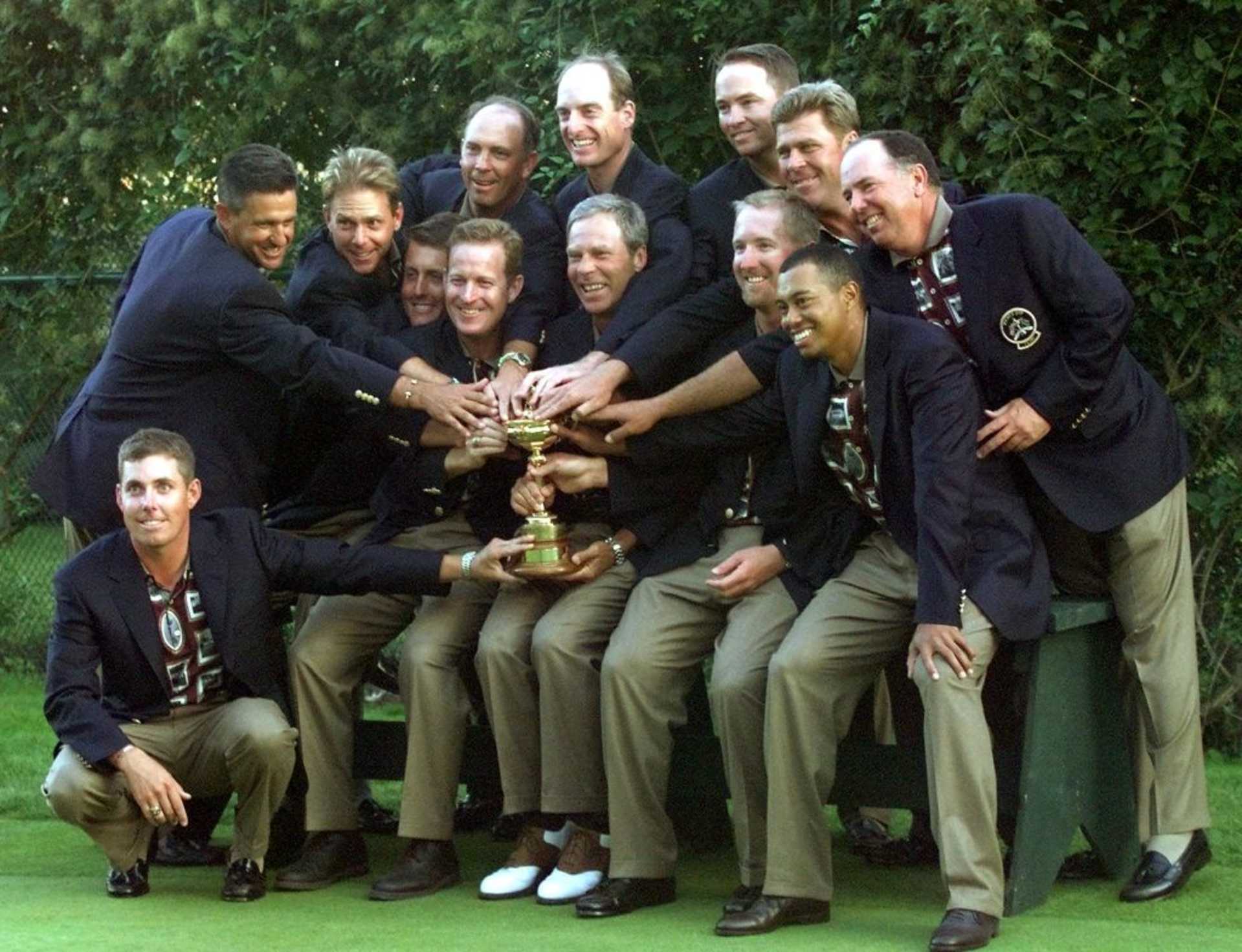 US Ryder Cup team members (L to R) Justin Leonard, (kneeling), Steve Pate, Payne Stewart, Phil Mickelson, Jeff Maggert, Captain Ben Crenshaw, David Duval, Tiger Woods, (back row) Tom Lehman, Jim Furyk, Davis Love III, Hal Sutton and Mark O'Meara touch the Ryder Cup during team pictures 26 September,1999 after winning at The Country Club in Brookline, Massachusetts. The US defeated the Europea team 14 1/2 to 13 1/2. (ELECTRONIC IMAGE)   AFP PHOTO/Timothy A. CLARY (Photo by Timothy A. CLARY / AFP) (Photo by TIMOTHY A. CLARY/AFP via Getty Images)