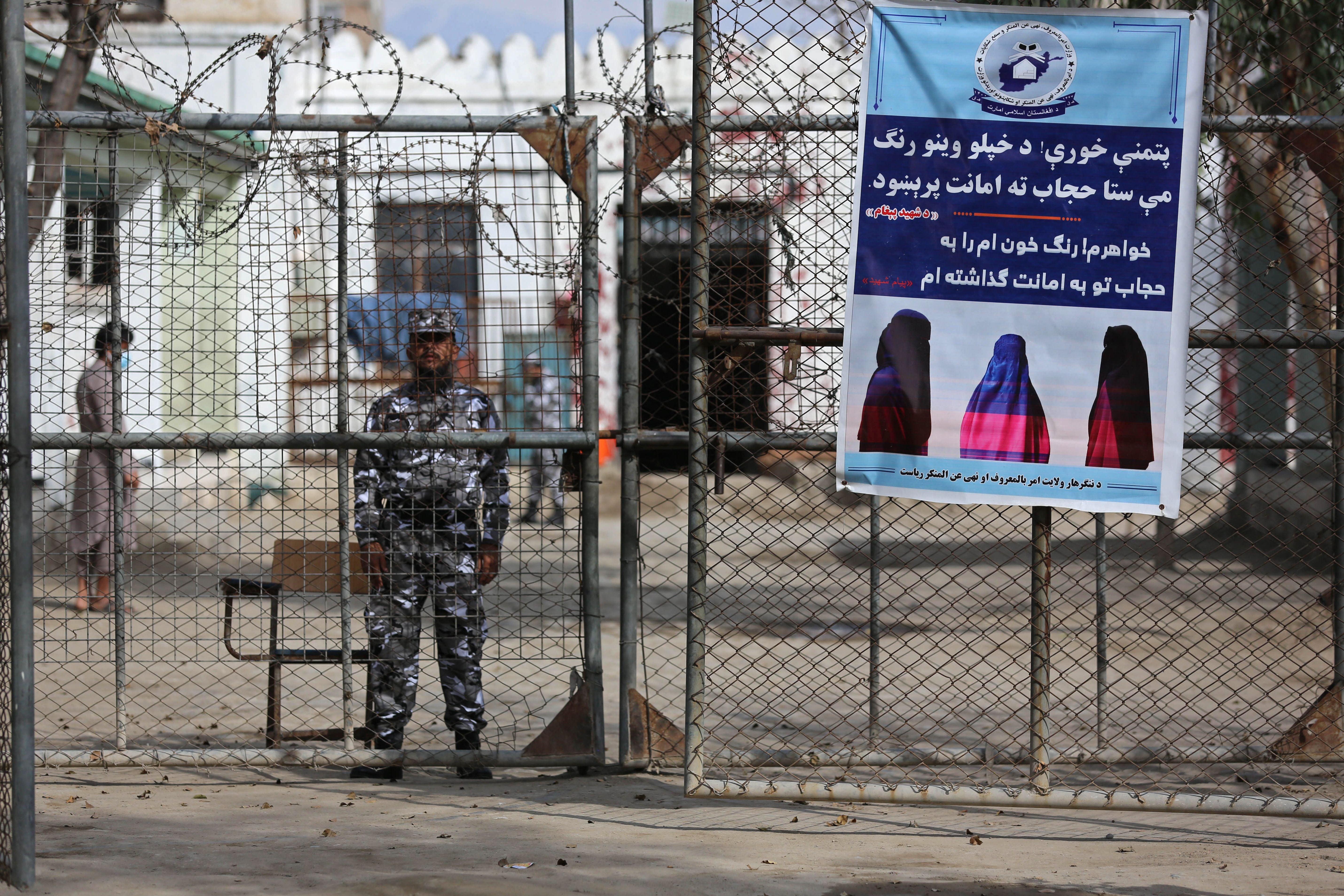 A Taliban prison security guard stands next to a poster ordering women to cover themselves with a Hijab during the distribution of new uniforms' ceremony by the Taliban authorities at a prison in Jalalabad
