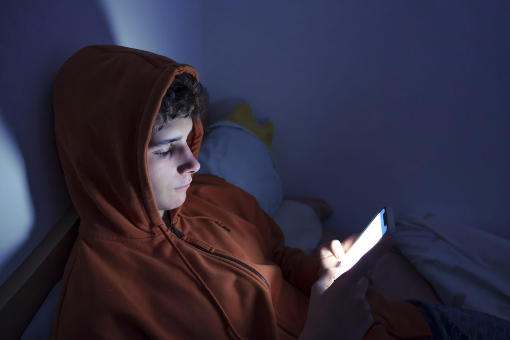 Teenager using a smartphone lying in bed late at night