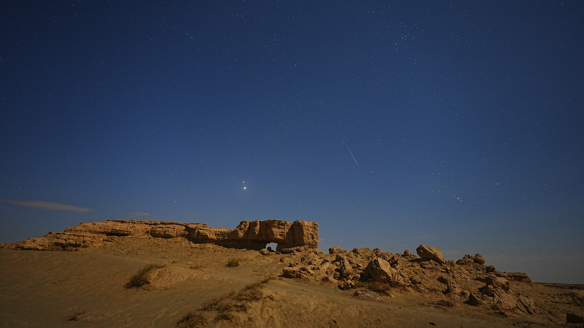 A meteor is pictured streaking through a starry night sky above a rocky outcrop.