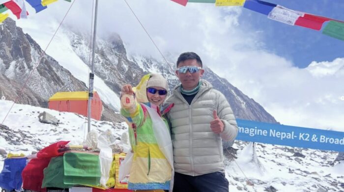 The climbers pose standing up at K2 Base Camp with a chortent and tents behind.
