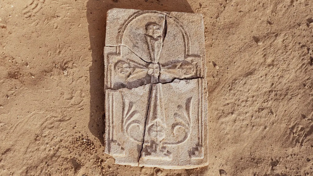 a plaster panel with a Christian cross sits partially broken on orange colored dirt