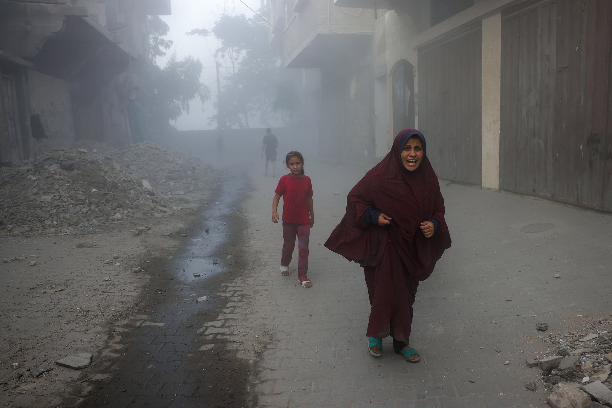A Palestinian woman and children run from the site of Israeli air strikes near Jabalia in northern Gaza on Tuesday