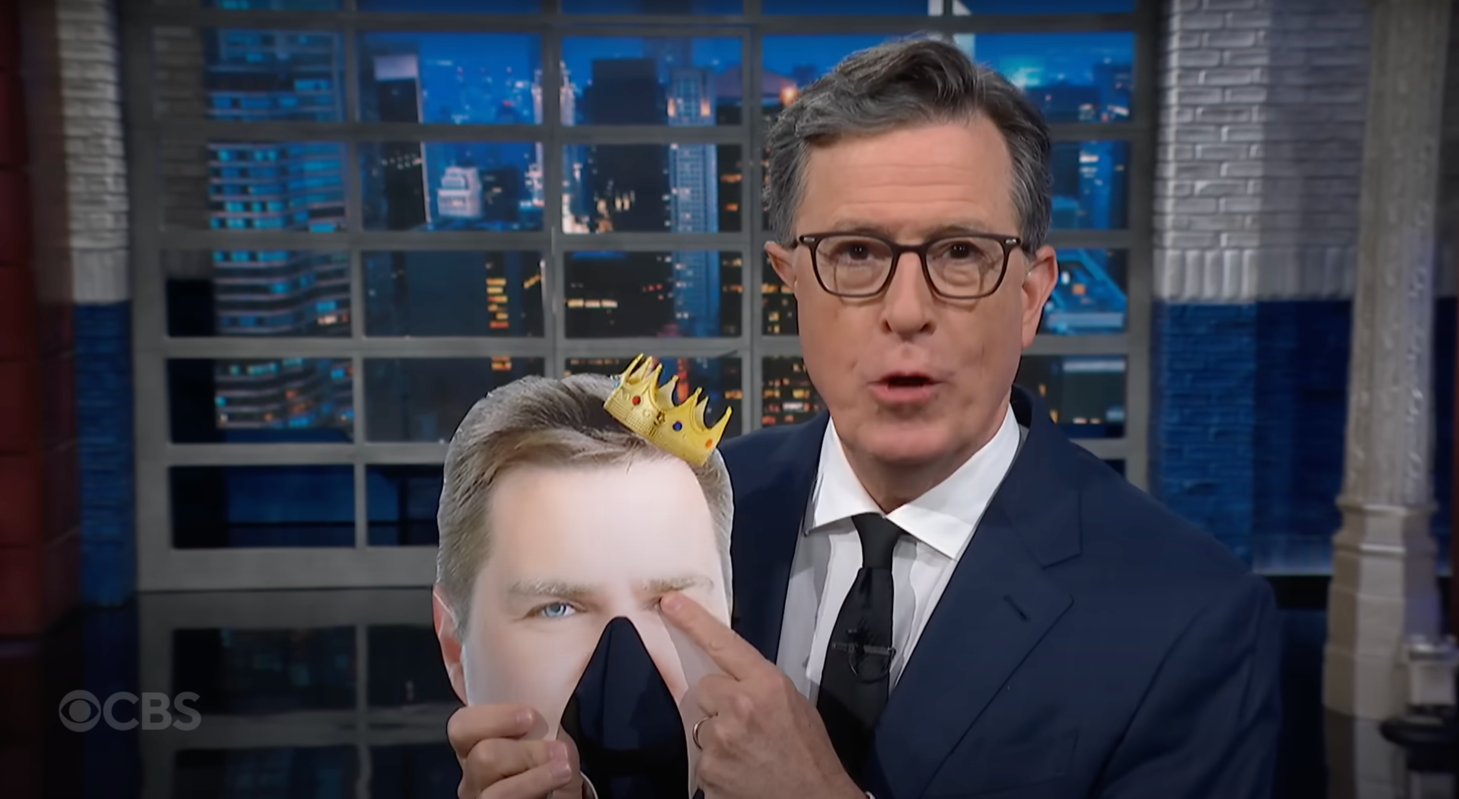 Stephen Colbert holding a JD Vance mask