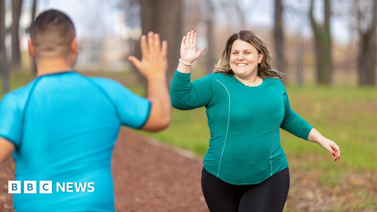 A woman runner gives a man a high five as she jogs past him in the park