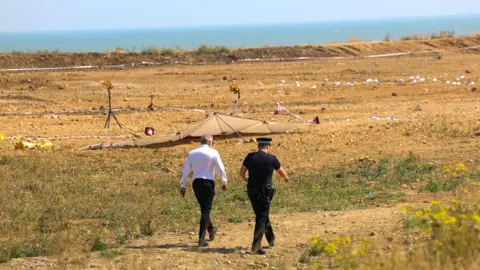 UKNIP A police officer and a man in a white shirt walk towards the crime scene, which on a dune just off the beach.