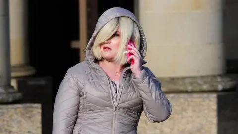 Spindrift Isla Bryson, with blonde hair and a grey hooded jacket, speaks on a phone outside court. 