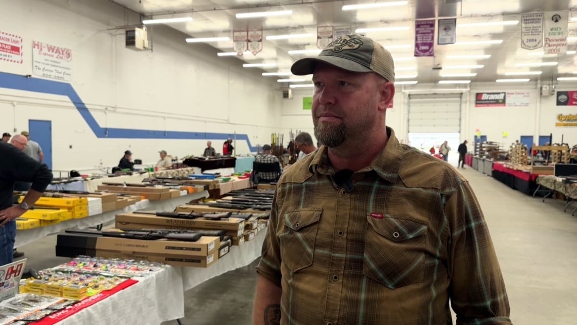 A man wears a plaid shirt and baseball cap in a hall.