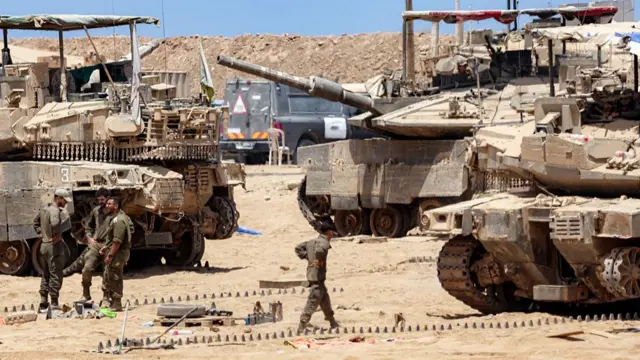 Israeli army soldiers perform maintenance tasks near main battle tanks positioned near the border with the Gaza Strip