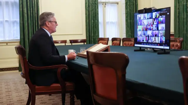 UK Prime Minister speaks into a virtual meeting. The screen of the computer shows other leaders' headshots as they take part in the call