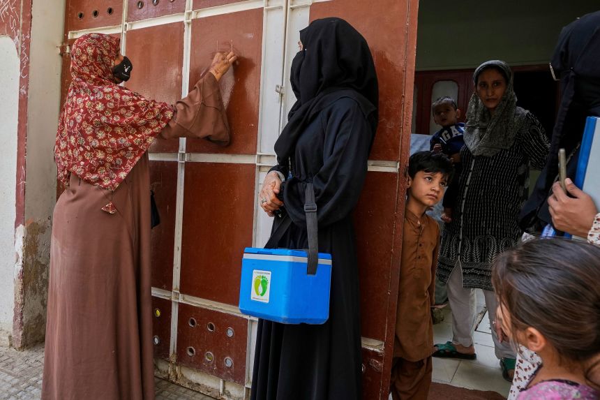 A health worker, left, marks a house after administering polio vaccines in Karachi, Pakistan, in April.