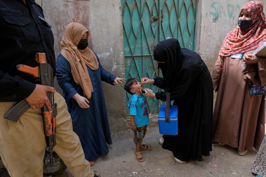 A police officer stands guard while a health worker, center, administers a polio vaccine to a child in Karachi, Pakistan, in April.