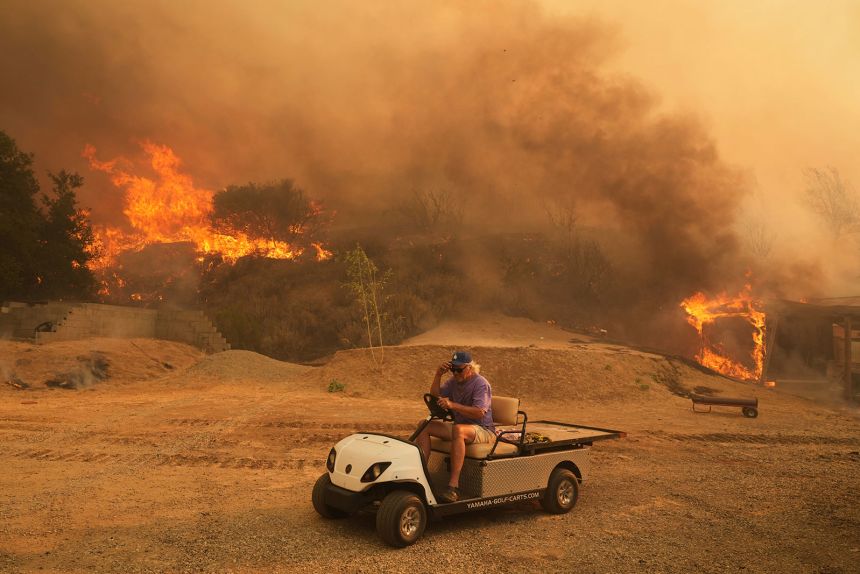 A resident rides a golf cart as he exits his property while the Canyon Fire burns on Thursday in Halsey Canyon, California.