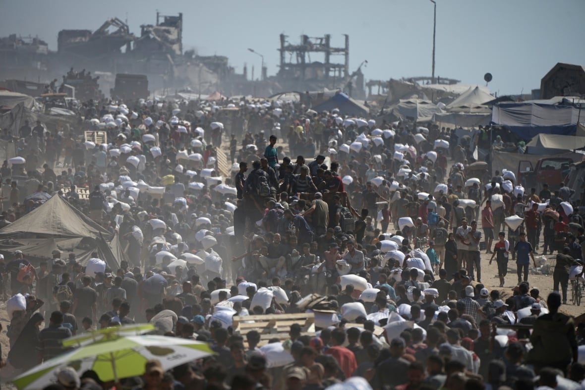 A large convoy of people carry white sacks as they march along a road.