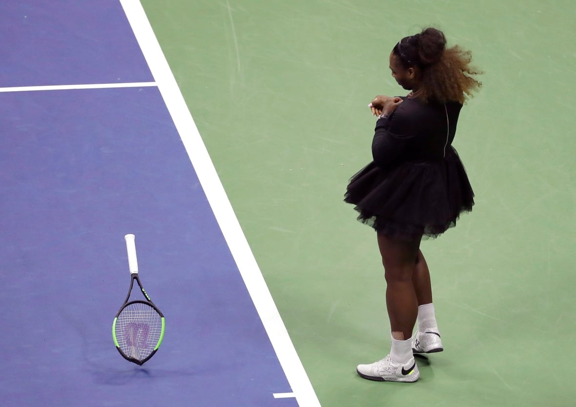 A woman dressed in black throws a tennis racket