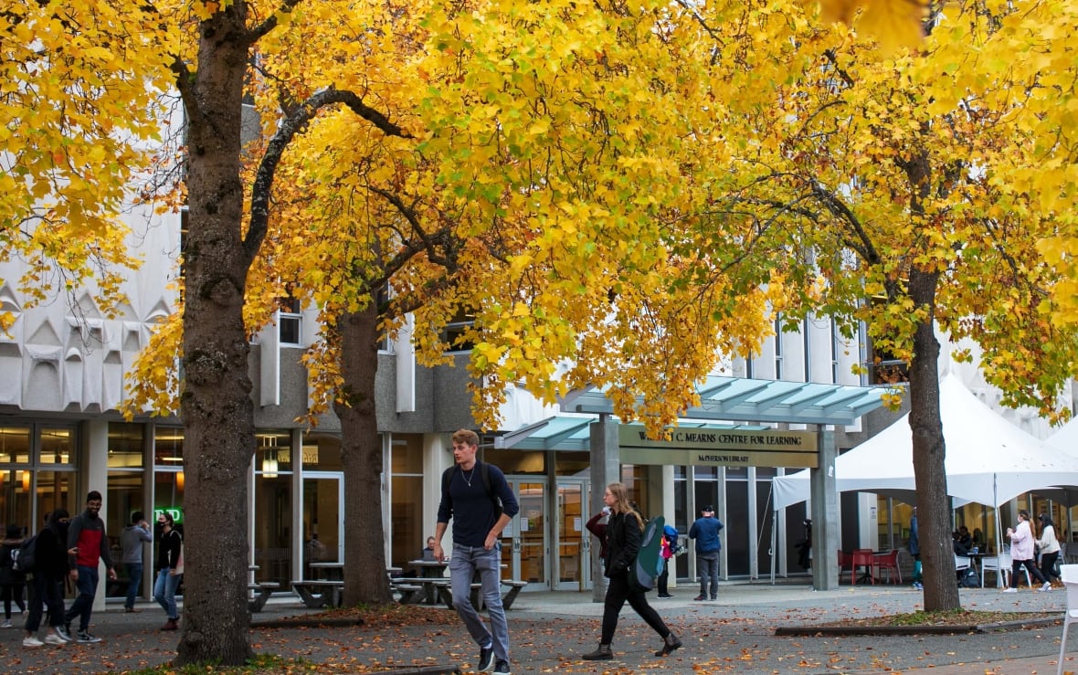 Students walk under trees on the campus of the University of Victoria.