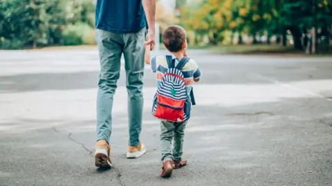 Getty Images A man holds the hand of a young boy as they walk with their backs to the camera.