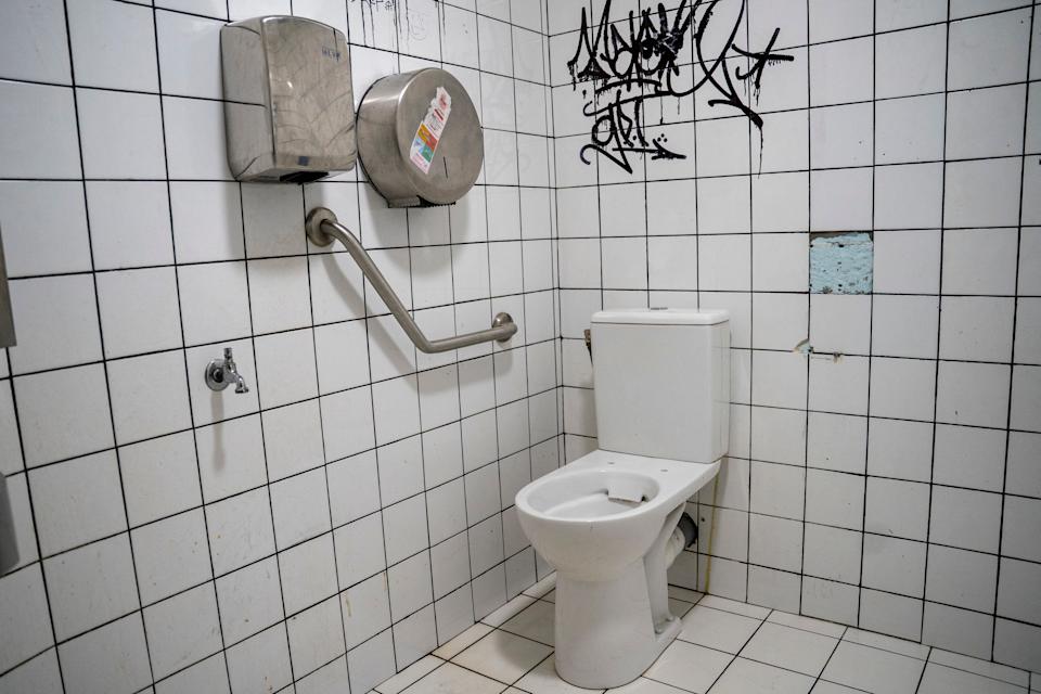A disabled toilet with graffiti on the wall, and a missing tile on the wall.