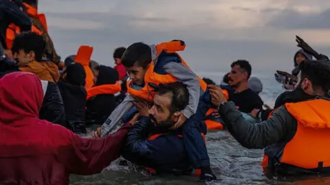 Getty Images Migrant families wade into the sea in an attempt to board a small boat on 12 August 2025 in Gravelines, France.