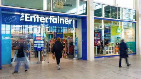 The Entertainer The Entertainer store front in an indoor shopping centre with blurred customers walking past