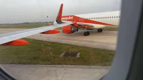 Phil Aspin Image taken from a plane window shows the other orange and white liveried EasyJet plane on another taxiway. Both taxiways are joining together at a junction where their wings have clipped.