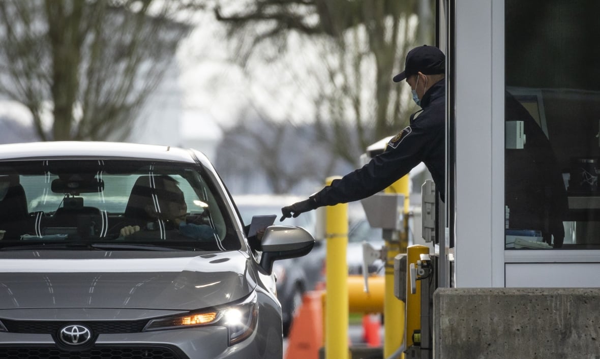 An officer at a border crossing reaches out to get someone's documents from a car window.