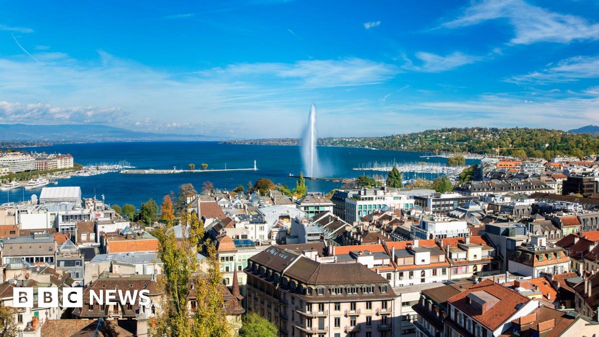 Switzerland's president Karin Keller-Sutter smiling sat at a desk with a blue background and part of a swiss flag behind her